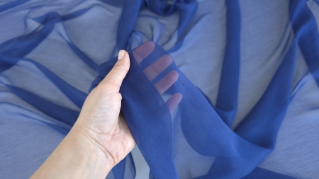 Mână care ține material transparent albastru închis arătând gradul de transparență