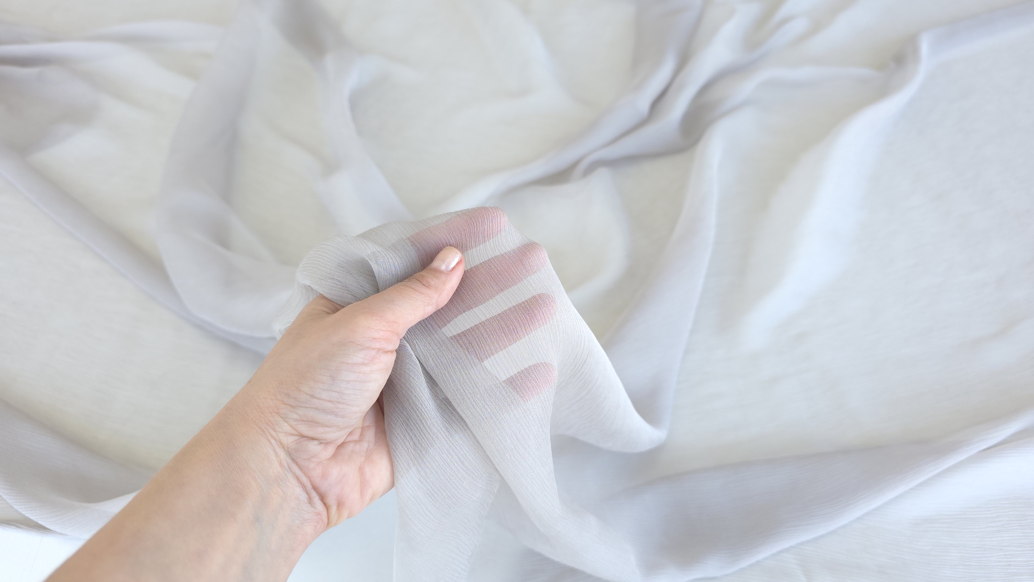 Mână care ține material transparent cu degetele vizibile prin țesătură subțire