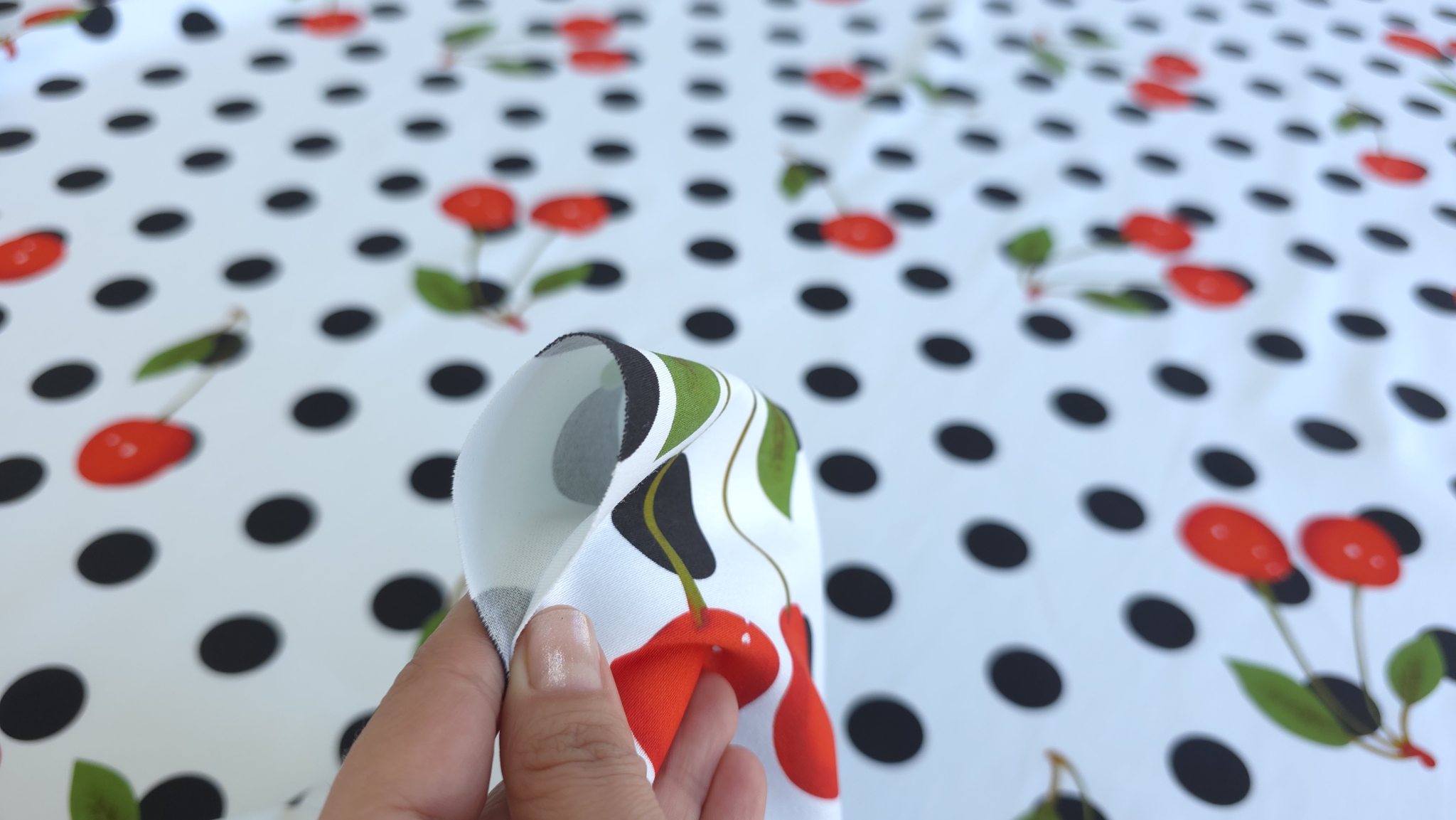 Mână ridicând colțul materialului cherry arătând dosul cu imprimeu estompat