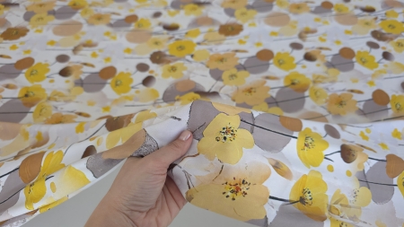 Mână ridicând colțul satinului floral galben arătând dosul mat al materialului