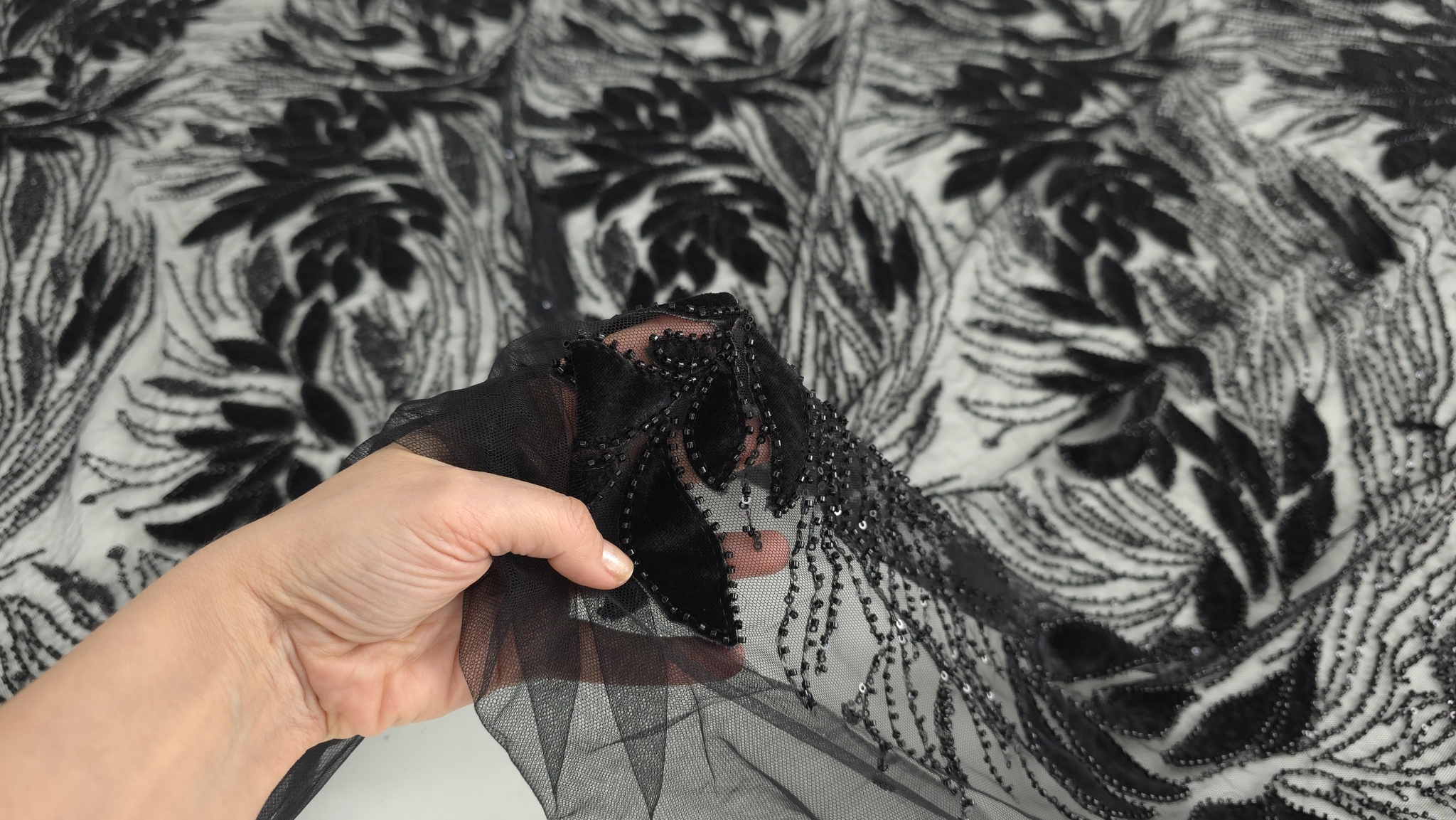 Mână ridicând materialul brodat, detaliu al fixării margelelor pe contururi