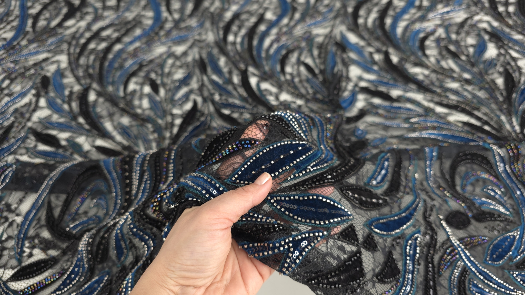 Mâna ridicând materialul cu tulle ul negru și desenul floral vizibil prin transparență