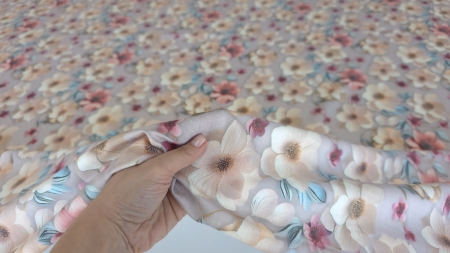 Mână ridicând ușor țesătura florală mauve gray cu textură fină și reflexii sidefate