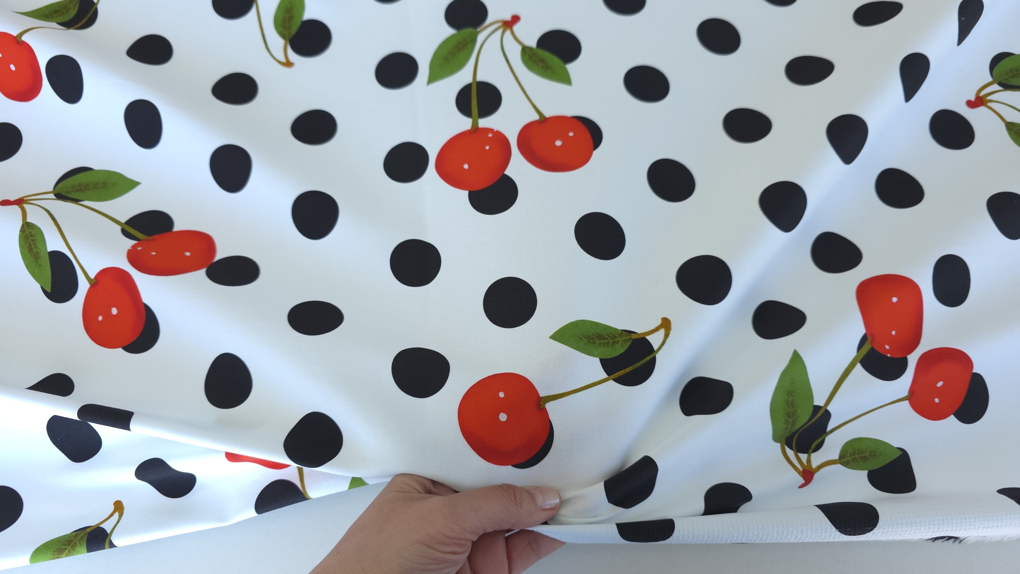 Mână strângând denimul elastic cherry formând falduri radiante cu buline și cireșe vizibile