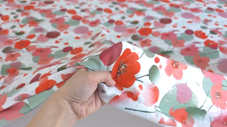 Mână strângând marginea materialului floral cu boboci roșii și pete de coral