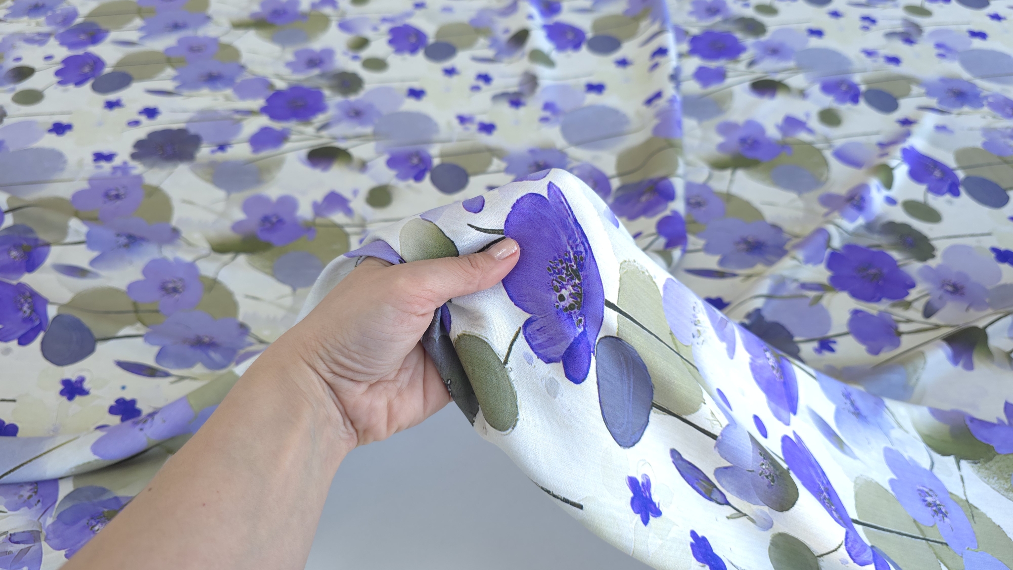 Mână strângând ușor materialul satinat cu imprimeu acuarelă floral pentru a evidenția textura fină