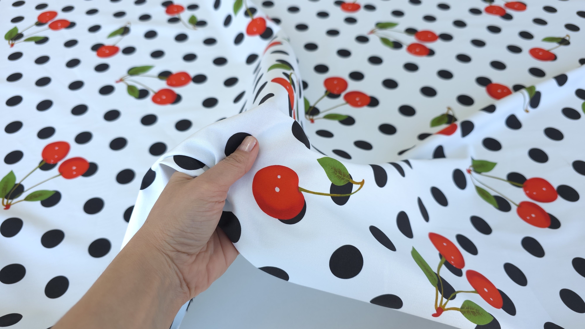 Mână ținând colțul materialului denim cherry cu cireșe roșii și buline negre în fundal