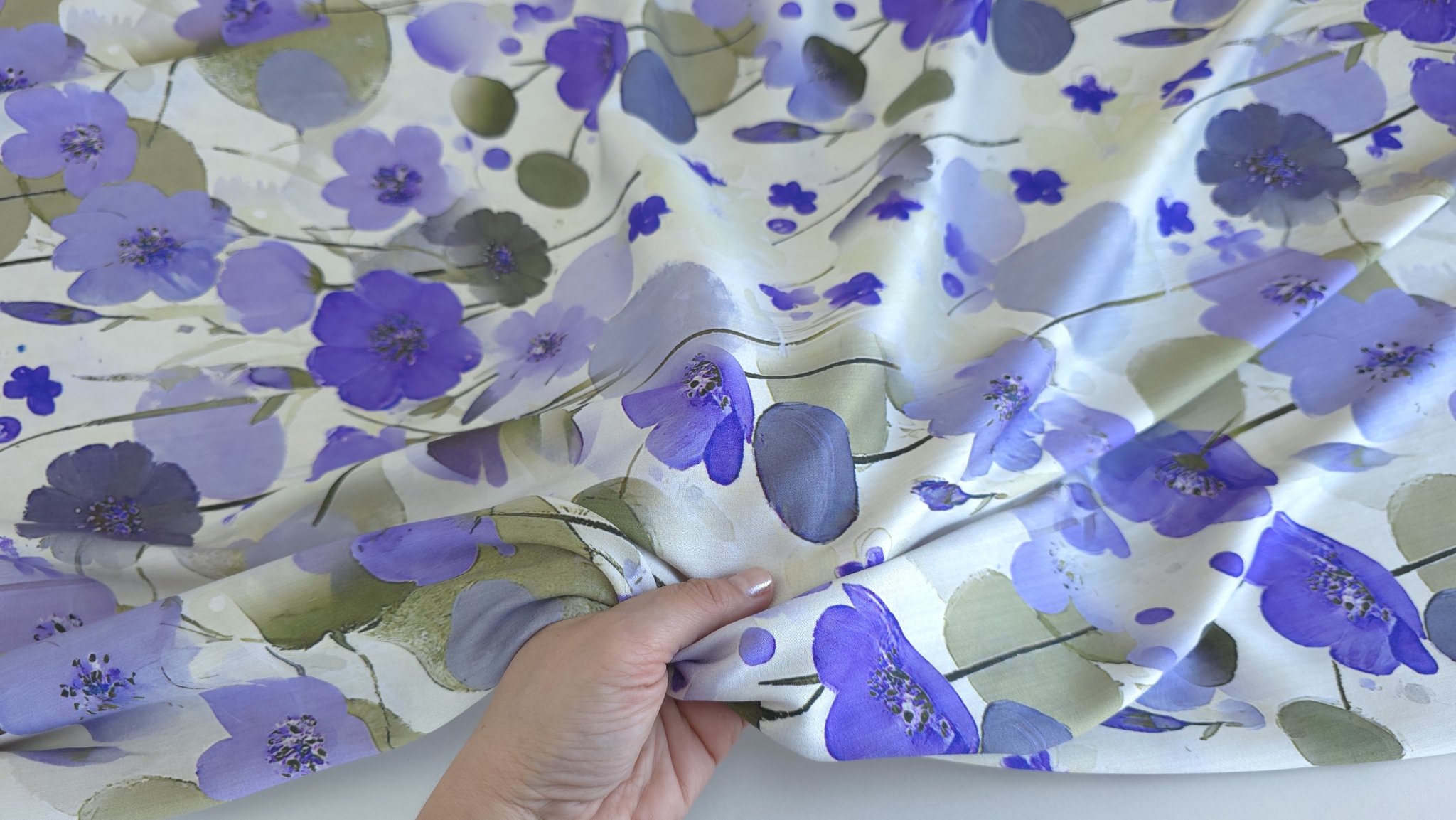 Mână ținând colțul materialului pentru a arăta căderea și textura fină