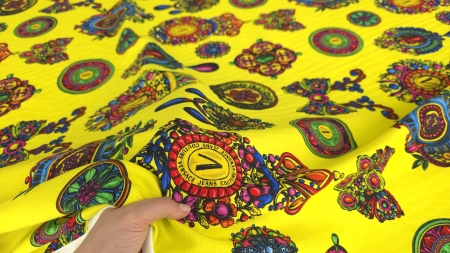 Mână ținând colțul țesăturii cu emblemă centrală ornamentală și medalioane colorate pe fond galben