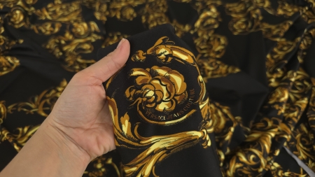 Mână ținând un pliu din jerseu cu motive baroce aurii pe fond negru