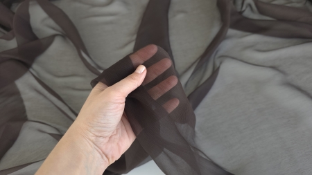 Mâna ținând voalul maro închis întins peste degete cu transparență clară a pielii vizibile