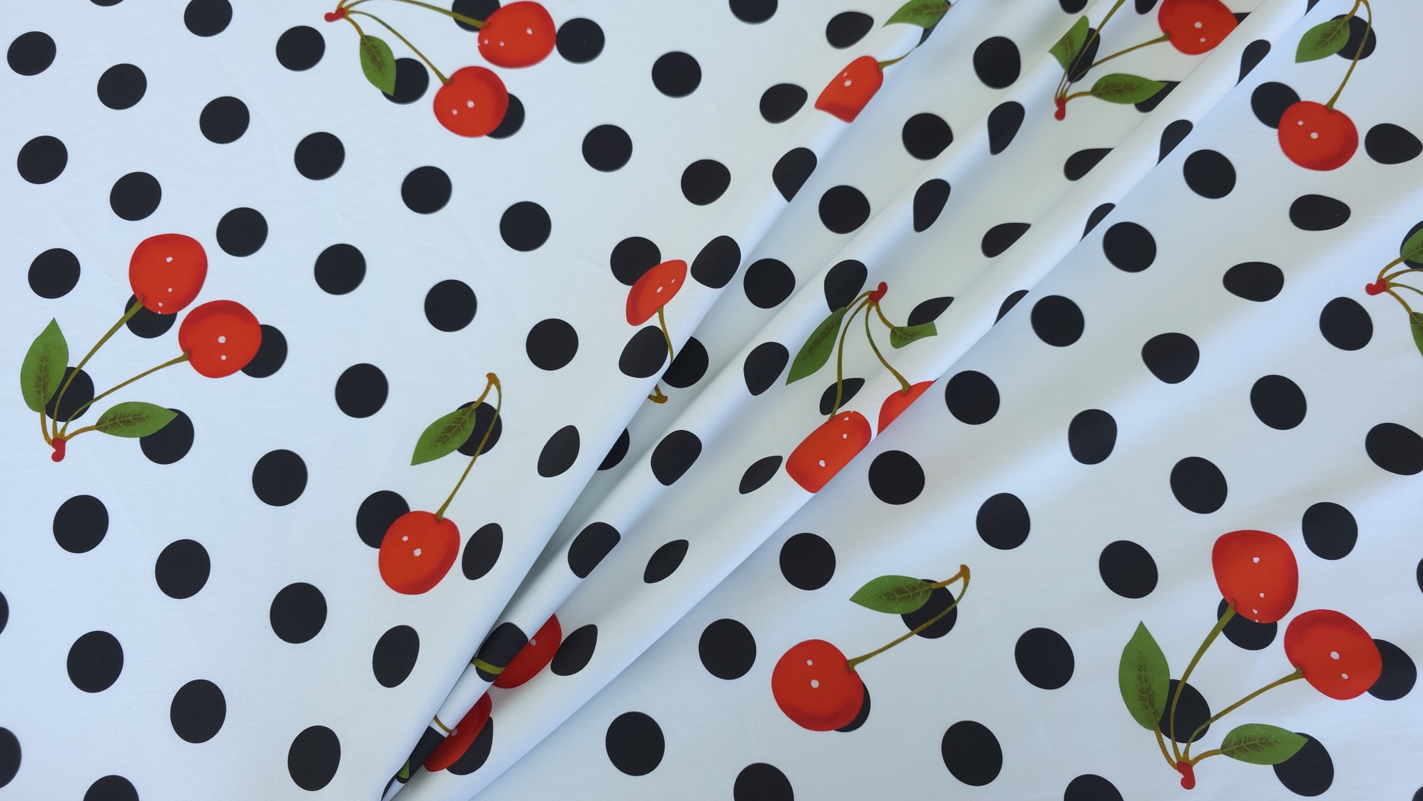 Material denim cherry desfăcut pe suprafață cu buline negre și perechi de cireșe presărate