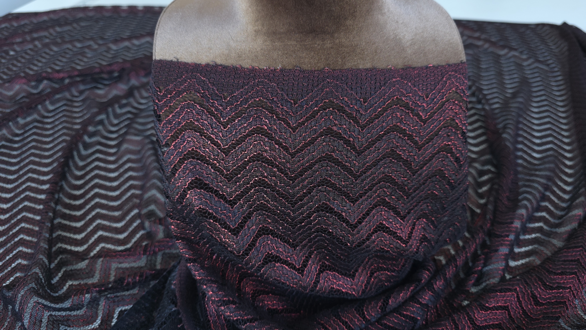 Material negru cu inserții roșii aranjat pe manechin în lumină laterală