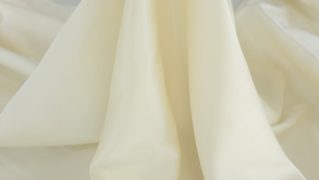 Material textil din mătase ivoire cu o cădere fluidă, formând falduri verticale elegante ce îi evidențiază luciul fin