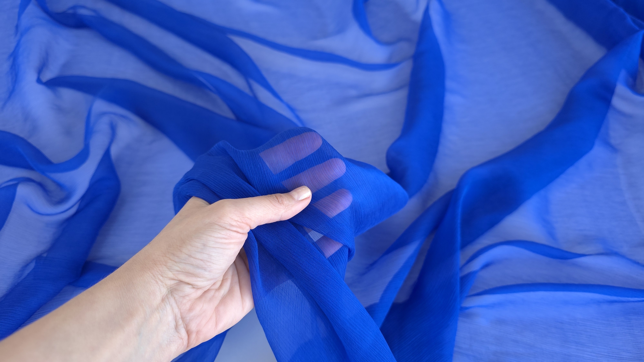 Mână care ține material transparent albastru arătând gradul de transparență