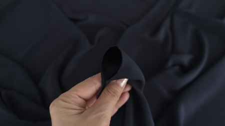 Materialul crepe de chine bleumarin ținut între degete evidențiind textura fină și opacitatea