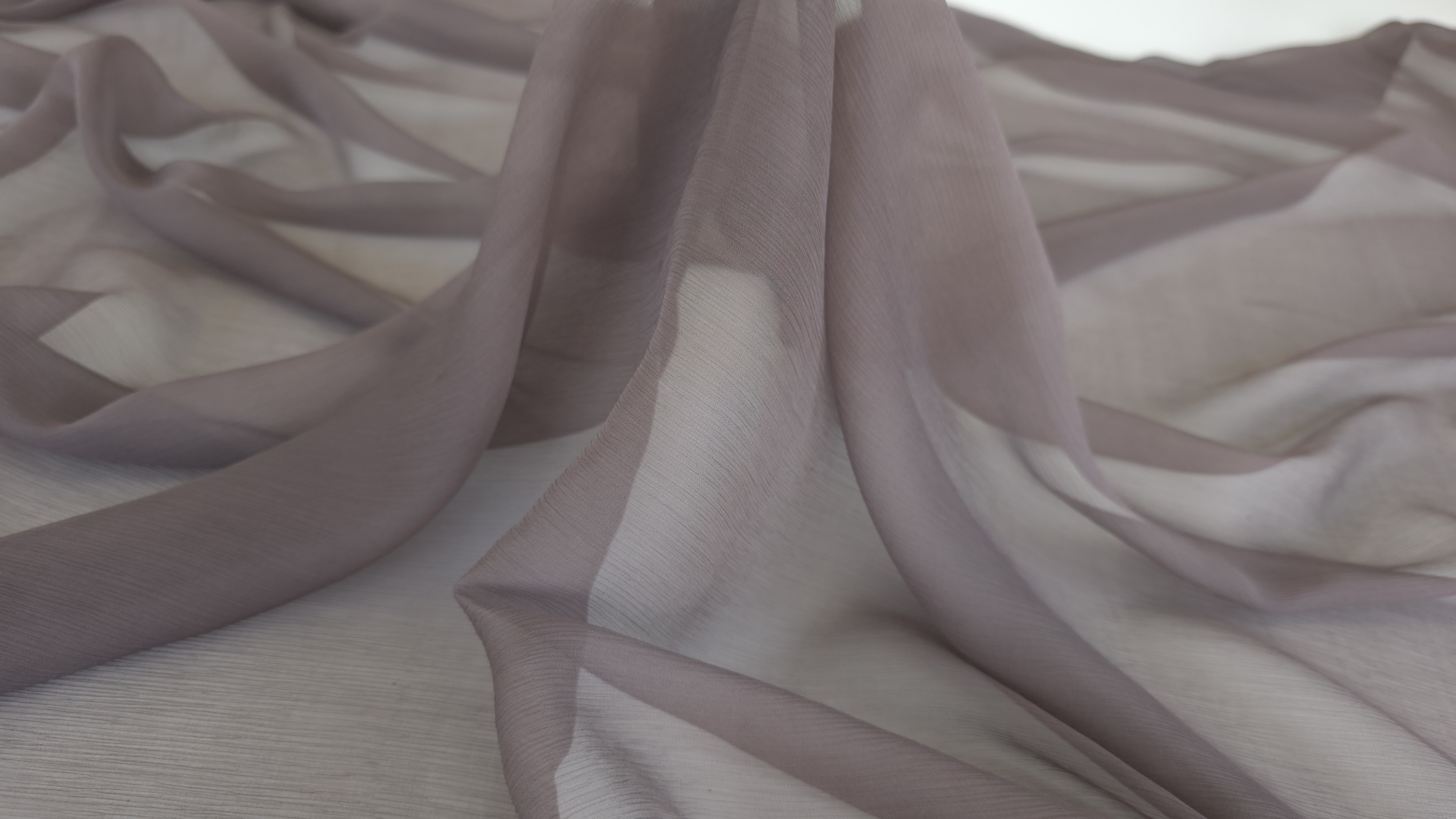 Materialul transparent cu nuanță caldă grej roz aranjat în falduri libere pe fundal alb