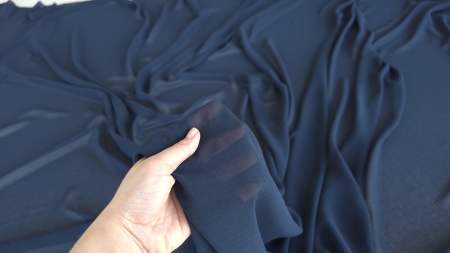 Metraj voal georgette bleumarin ridicat în mână cu degetele vizibile prin material