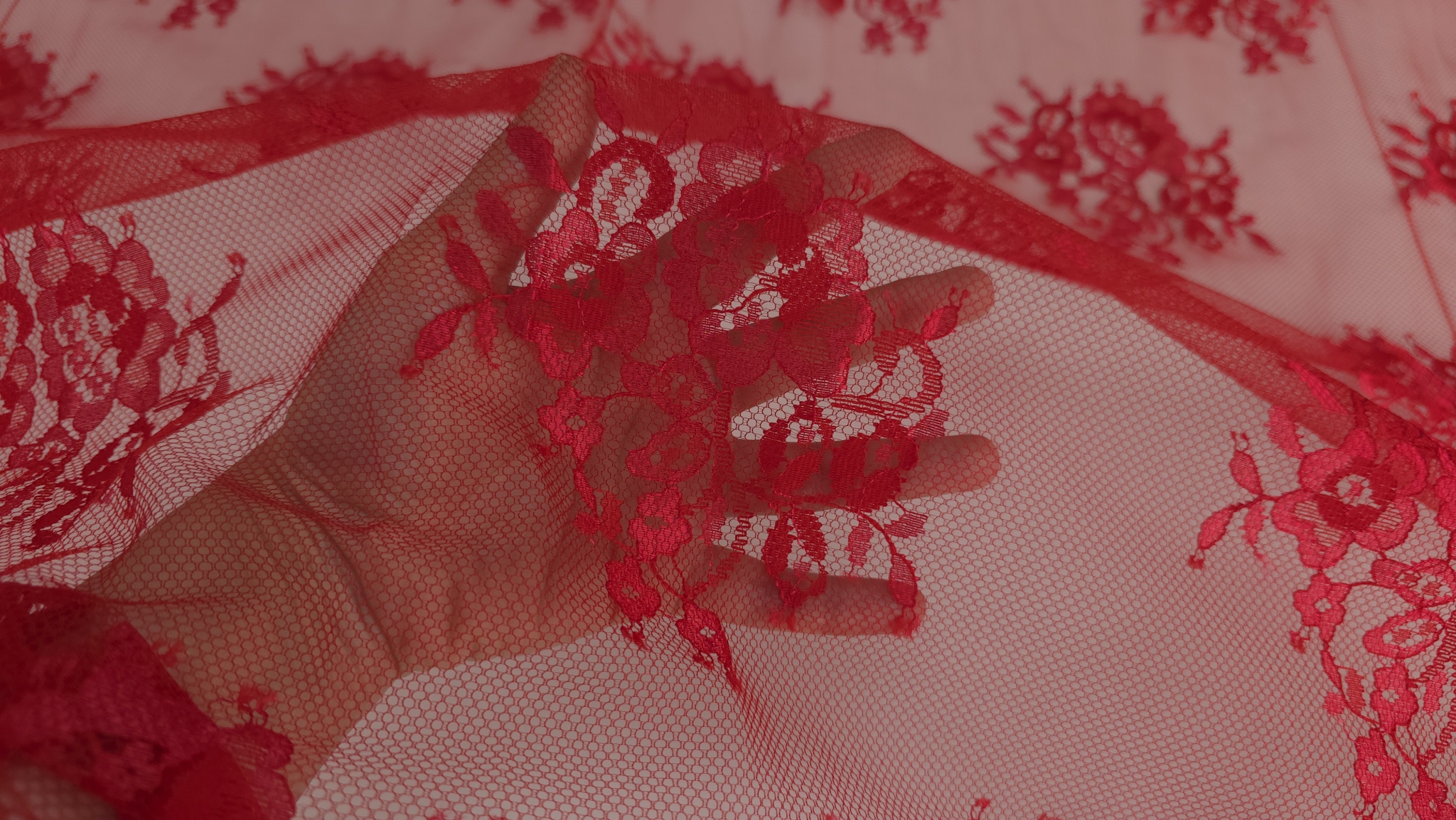Motiv floral Chantilly roșu Ferrari suprapus pe palmă evidențiind transparența tullului