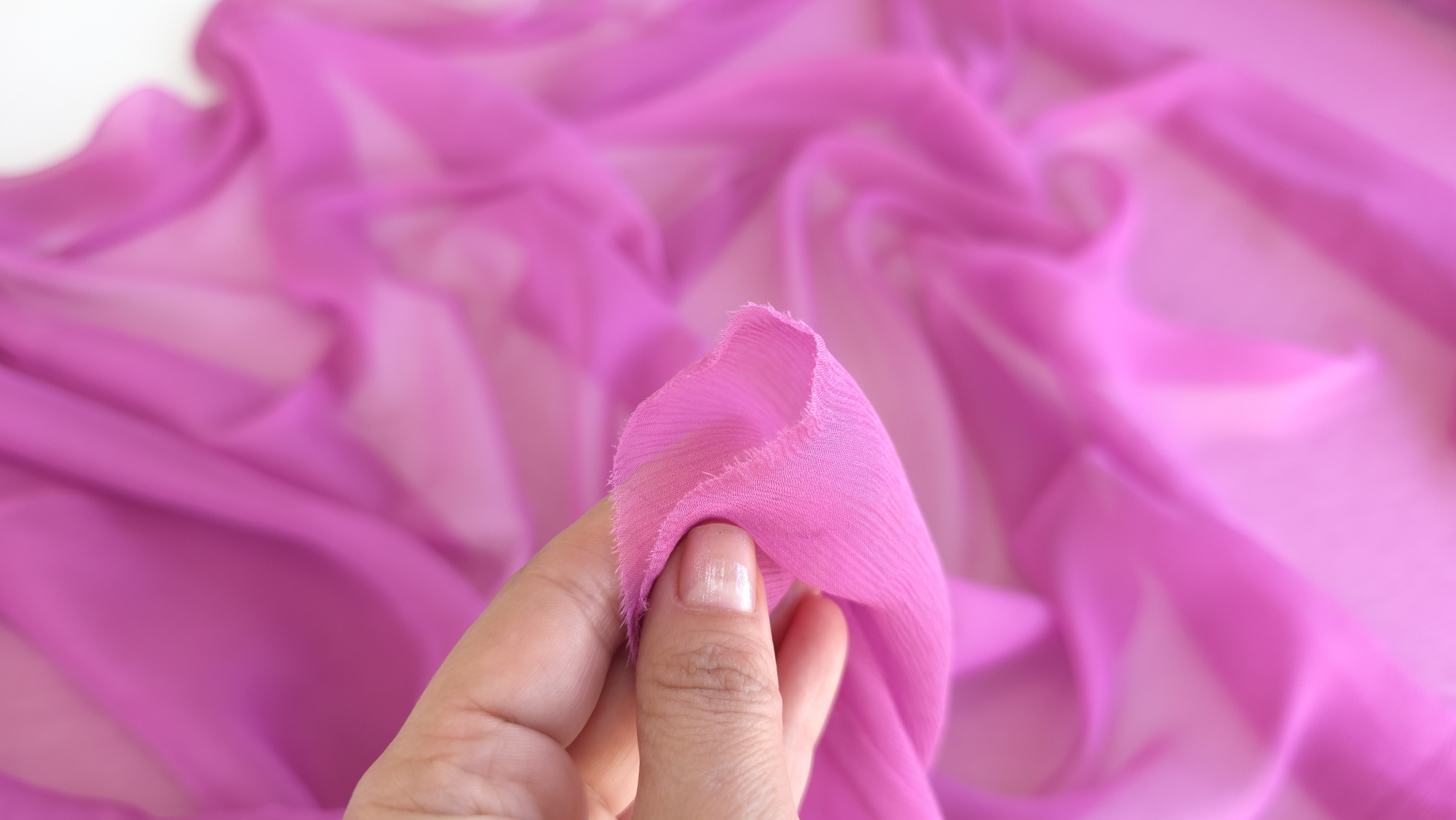 Muselină de mătase naturală roz zmeuriu ținută între degete cu transparență vizibilă