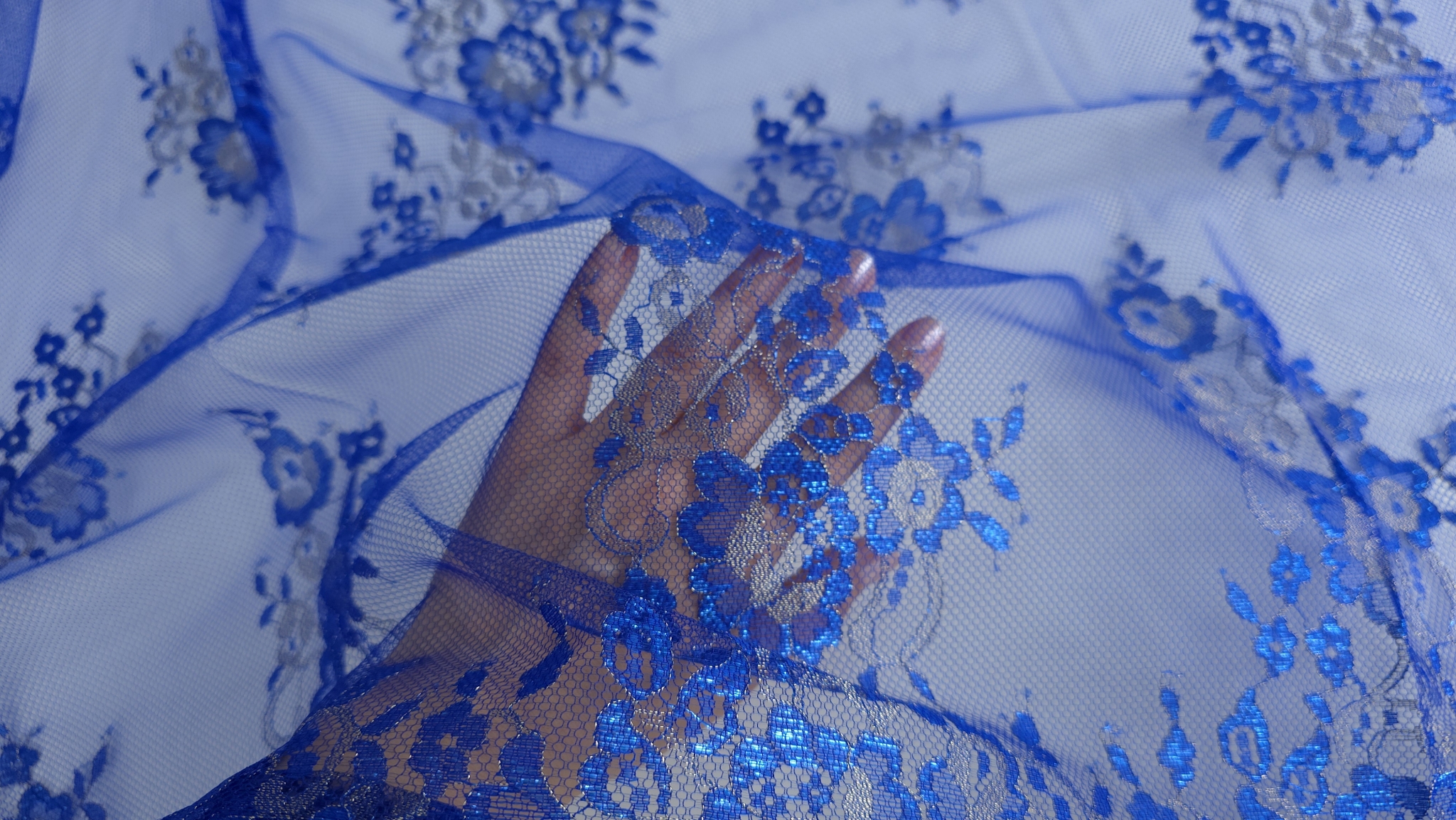 Palmă sub material transparent cu motive florale brodate și reflexii metalice vizibile prin tull