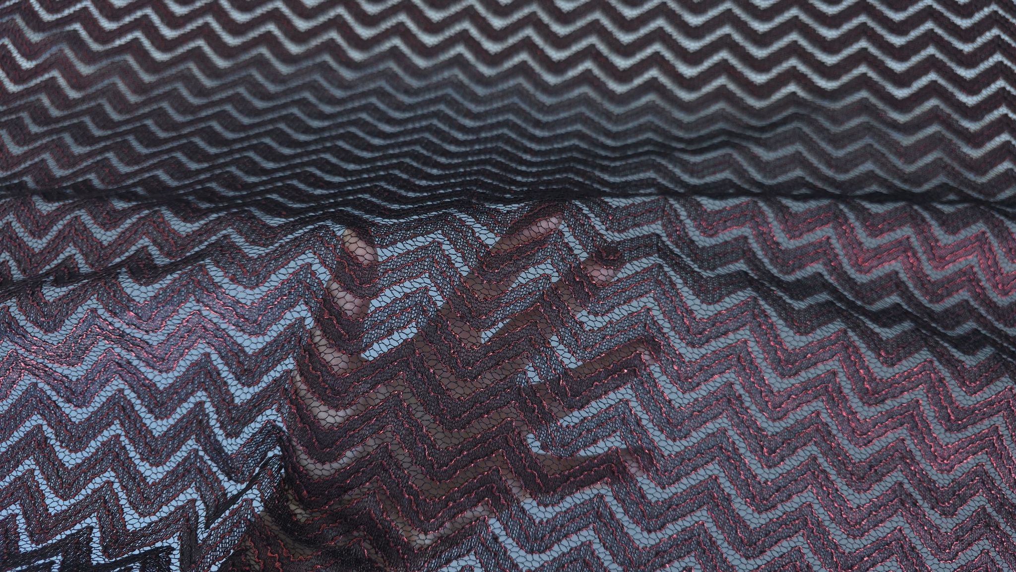 Plasă neagră cu zigzag roșu ridicată cu mâna pentru a arăta transparența ochiurilor