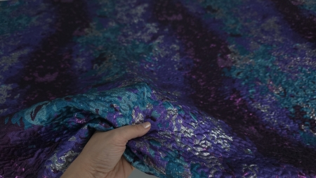 Țesătură densă ținută în mână cu falduri mov și reflexii argintii