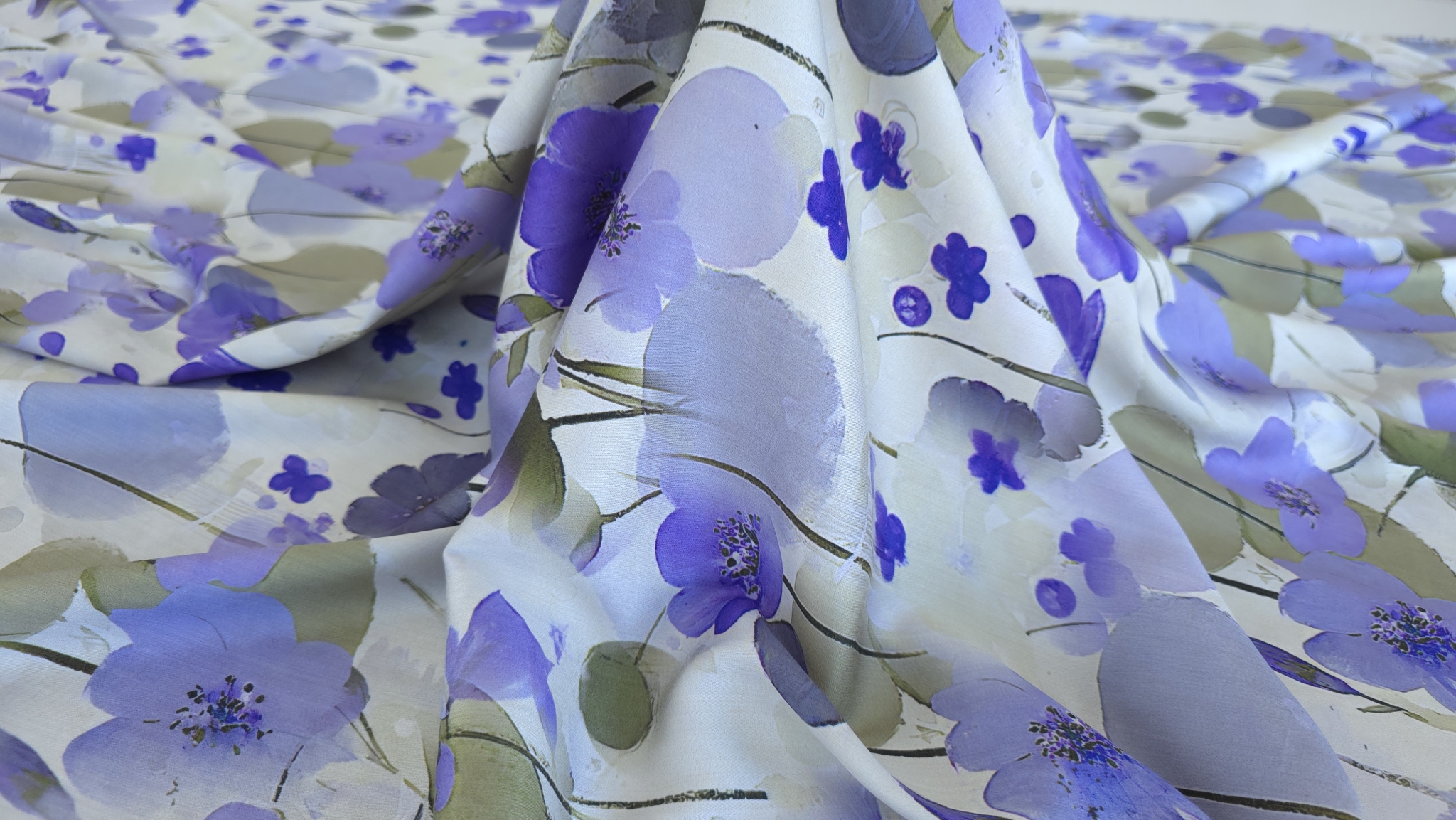 Țesătură satin vâscoză cu flori mov formând falduri ample și cădere fluidă pe masă