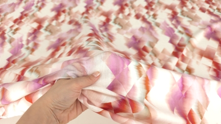 Țesătură vascoza print geometric roz și roșu cu falduri lejere pe suprafață deschisă