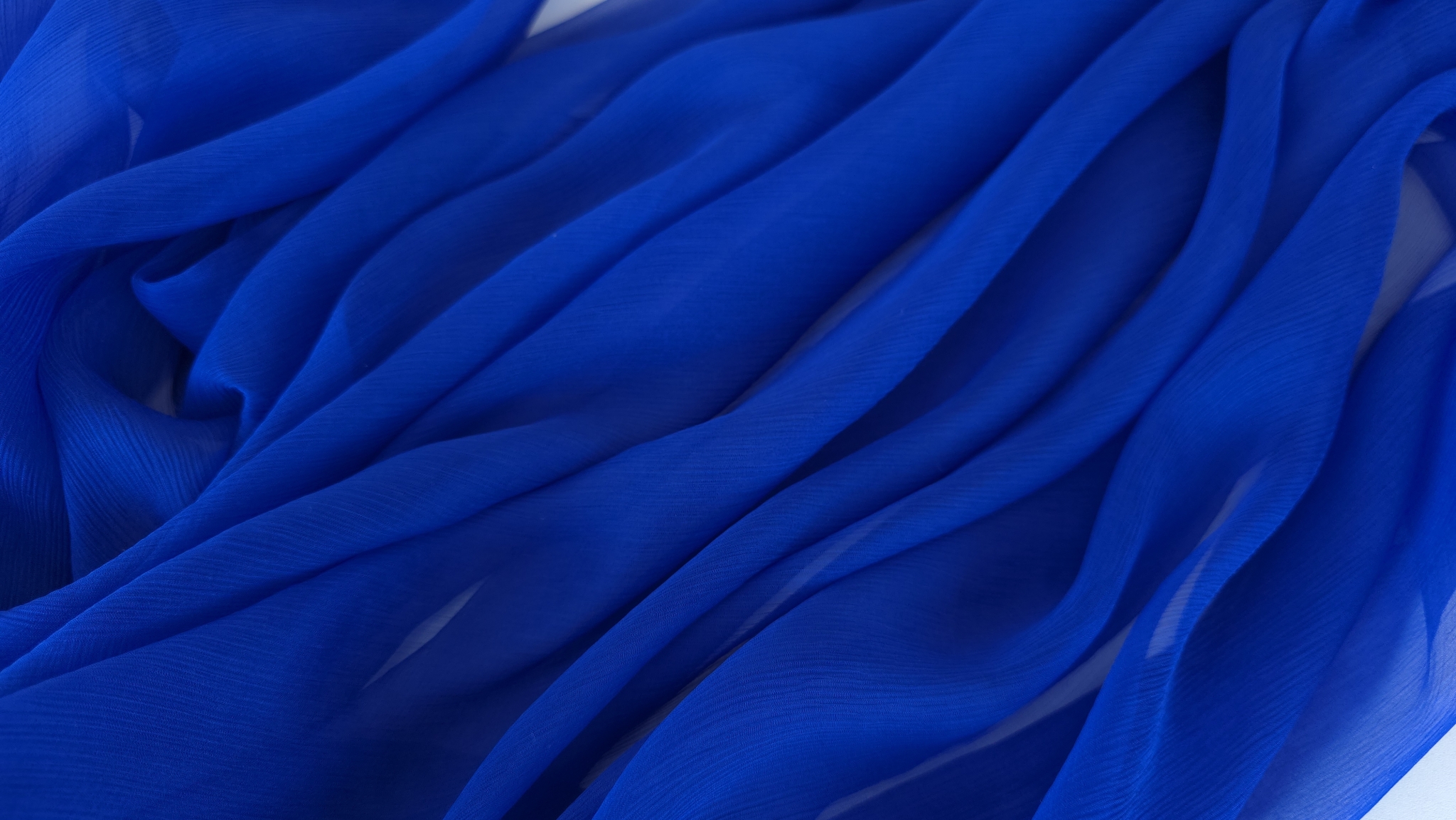 Voal creponat albastru cobalt din mătase naturală desfășurat pe suprafață albă