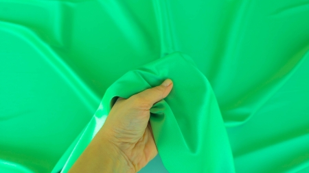 Mână care ridică un pliu vibrant de material verde proaspăt