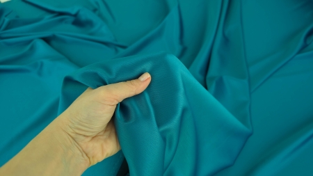 Mână care strânge în pumn material turcoaz falduri grupate căzute relaxat în jur