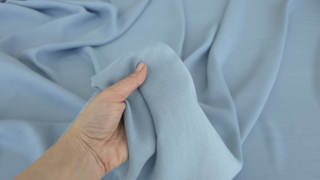 Mână ține material bleu pal răsfrânt, față și spate vizibile