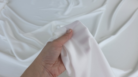 Material Regalia ivory alb prins în mână, falduri moi căzând lateral cu luciu satinat vizibil pe suprafață