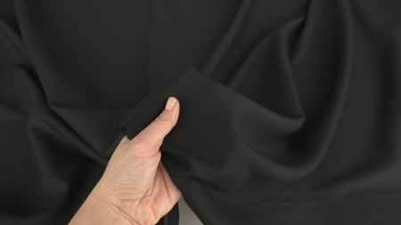 Material in negru cu elastan, ținut în mână, corp moderat vizibil