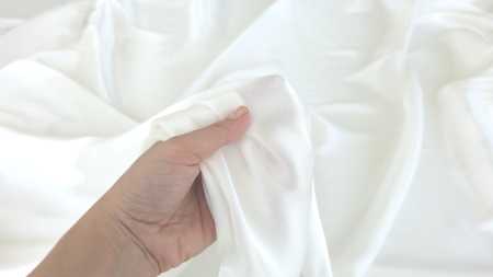 mână ridicând material fluid alb satinat cu falduri relaxate pe fundal deschis