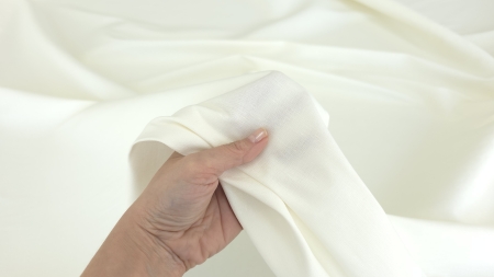mână strângând țesătură ivory cu falduri naturale relaxate în fundal deschis