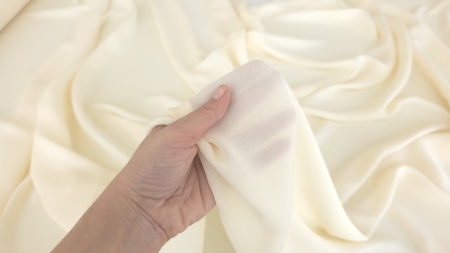 mână strângând țesătură ușoară ivory cu structură fină vizibilă în lumină