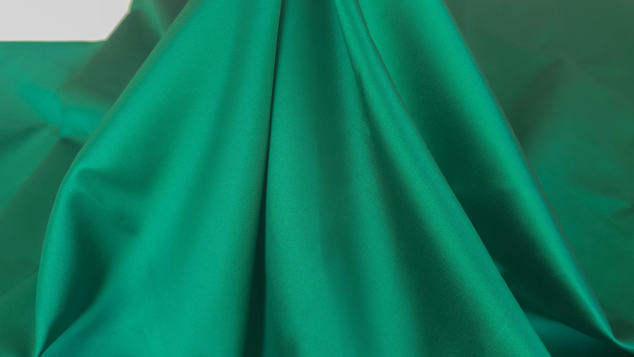 Față perlată și verso mat ale unui material verde intens, pliat geometric
