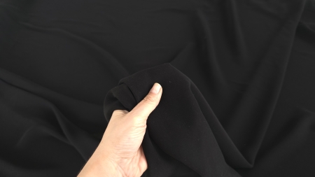Mână care prinde material crep negru mat, falduri controlate în jurul degetelor