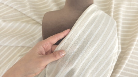 Mână ținând un pliu dintr-un material subțire în tonuri crem deschis