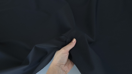 Material negru ținut în mână, falduri cu volum controlat, structură fermă vizibilă