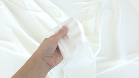 Satin elastic ivory cu matase la metru tinut in mana, transparenta usoara vizibila la capatul pliat, grosime fina