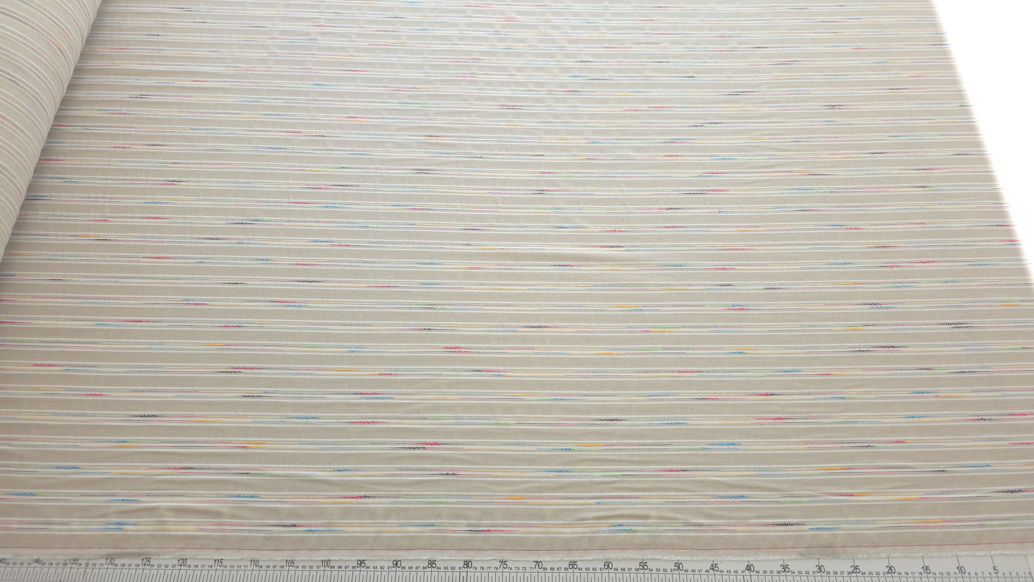 Țesătură cu in dungi ivory cu fir multicolor pe rulou cu riglă fond alb