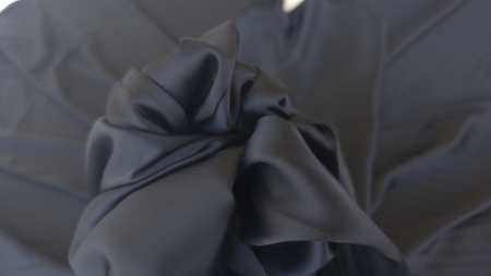 Material negru strans in mana cu cute adanci si contrast de lumina
