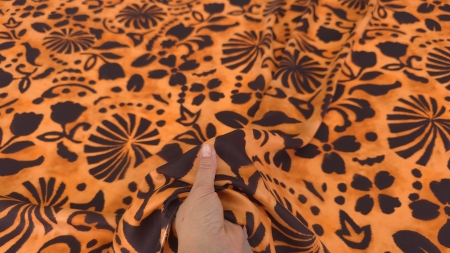 Material portocaliu cu flori negre in forma de evantai strans in mana