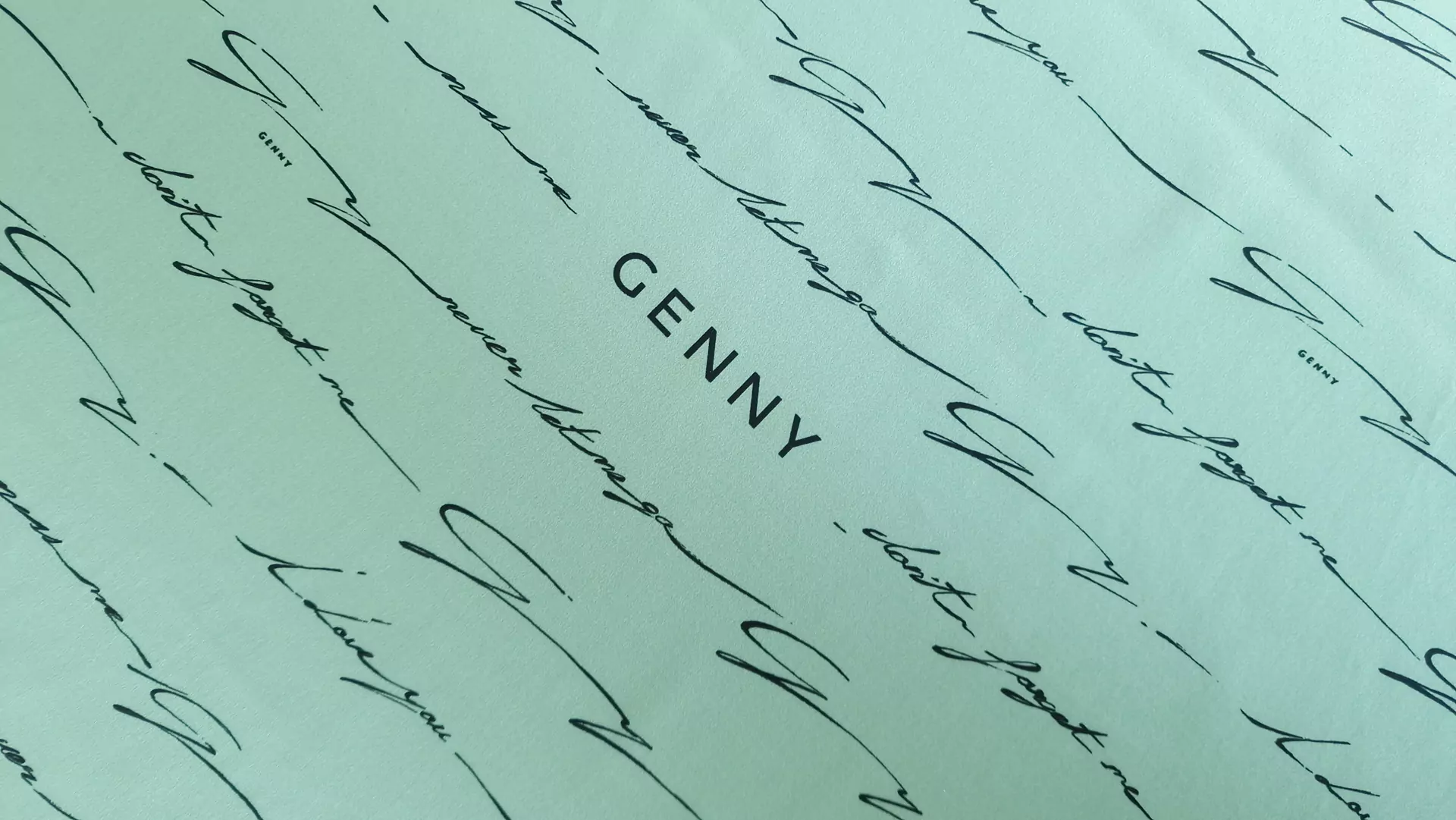 detaliu scris de mână cursiv negru și logo Genny pe fond mint