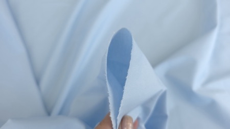 material bleu deschis tinut intre degete cu marginea taiata vizibila