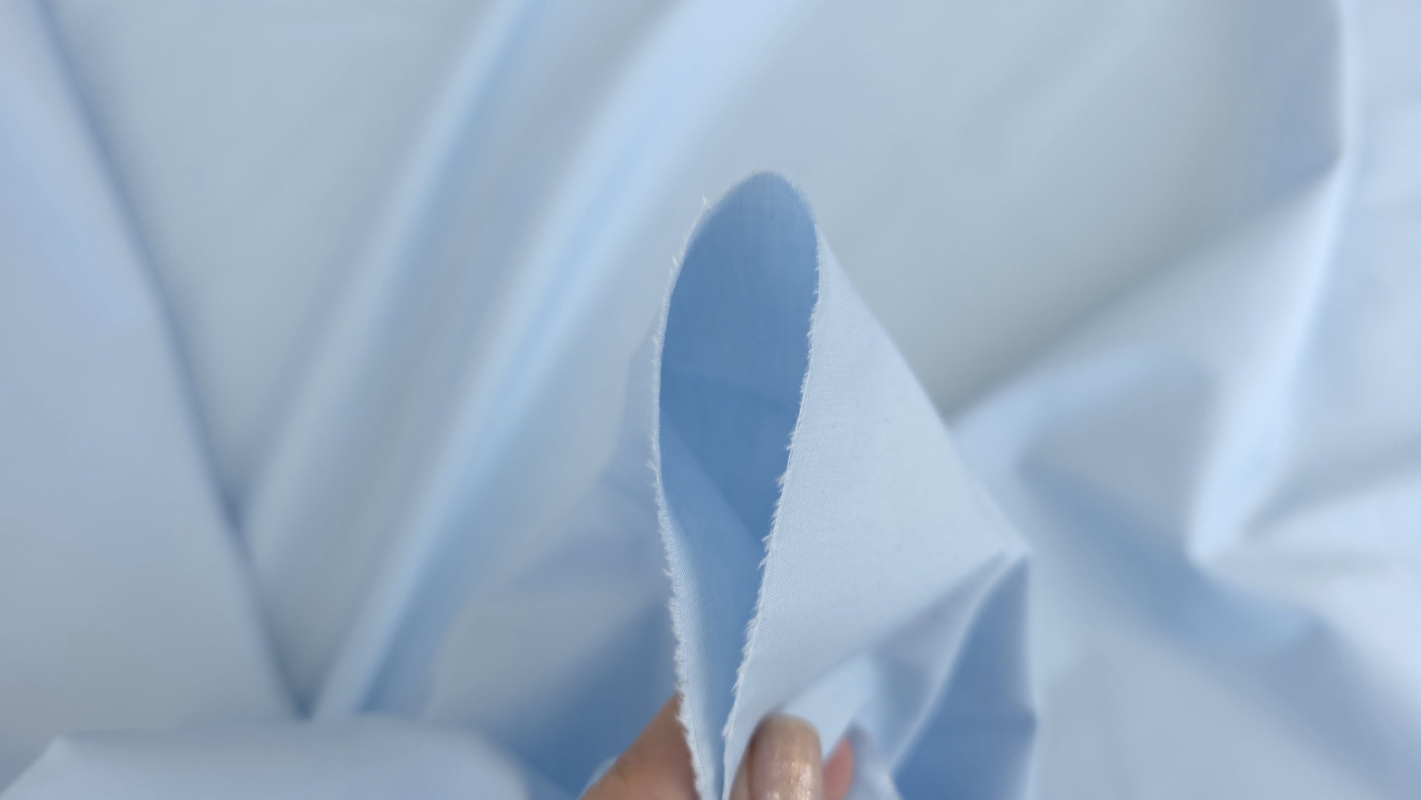 material bleu deschis tinut intre degete cu marginea taiata vizibila