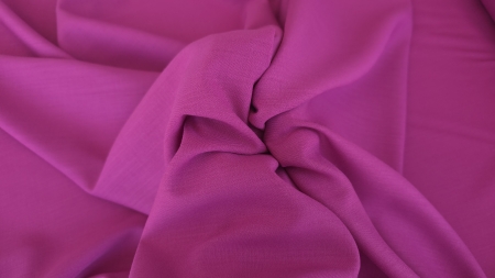 Material magenta strâns în mână, cu pliuri mici adunate în centru